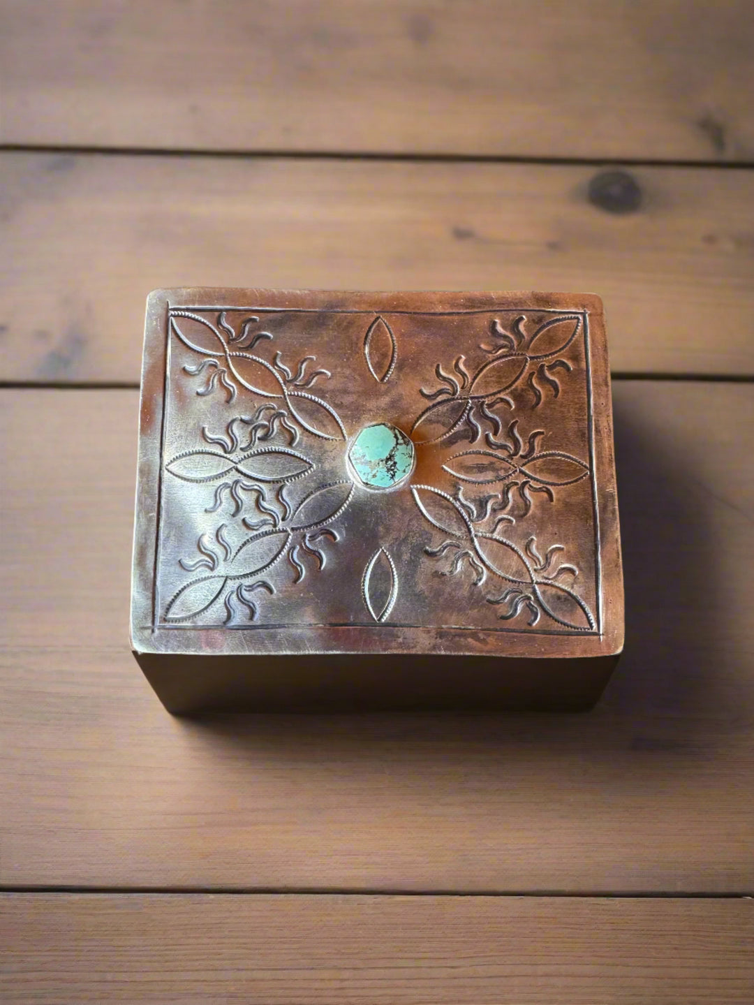 Decorative metal box with embossed design and turquoise stone on a wooden surface
