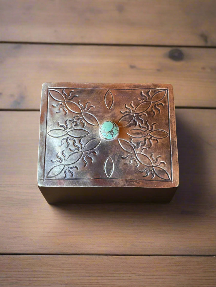Decorative metal box with embossed design and turquoise stone on a wooden surface